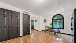 Um corredor com portas de madeira escura, uma placa com a palavra "PANTRY" e uma área de jantar com mesa e cadeiras.