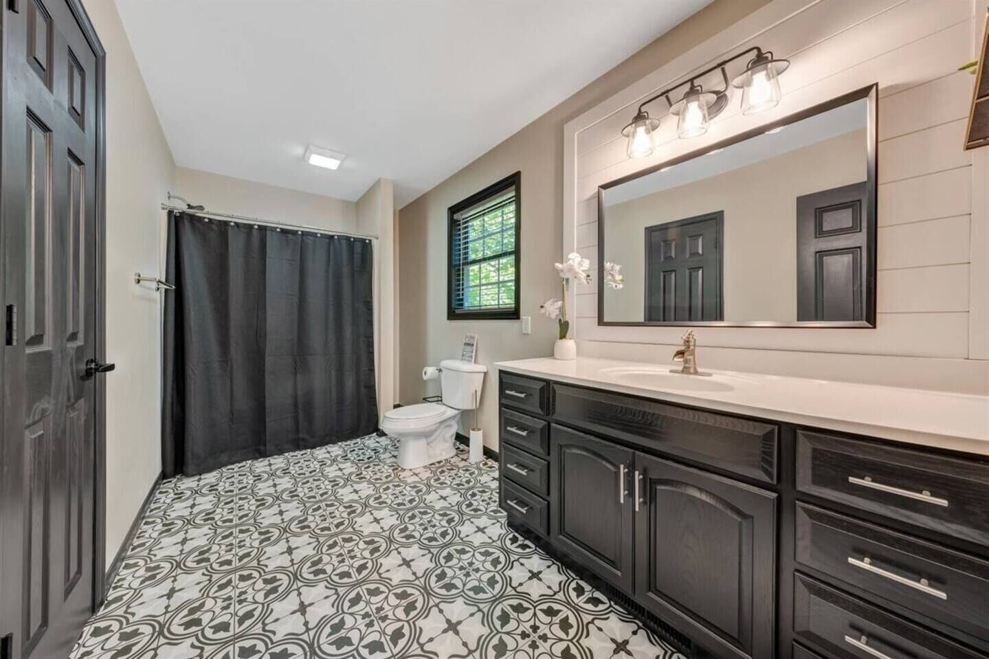 Une salle de bain avec un carrelage décoratif, des toilettes, un lavabo avec un miroir et des meubles sombres.