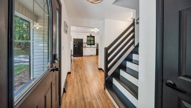 Um interior moderno com piso de madeira, escada com corrimão preto e área de cozinha ao fundo.