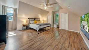 Quarto com uma cama grande, um ventilador de teto e uma janela com cortinas.
