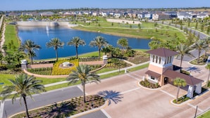 A golf course with a water feature, palm trees, and a building with a brown roof. - Townhome with Screened Pool, Kids Bedrooms, Near Attractions (Kissimmee)