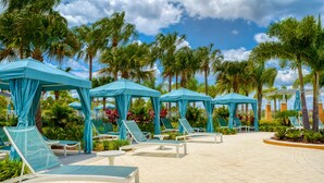 A poolside area with multiple blue canopies, white lounge chairs, and palm trees. - Townhome with Screened Pool, Kids Bedrooms, Near Attractions (Kissimmee)