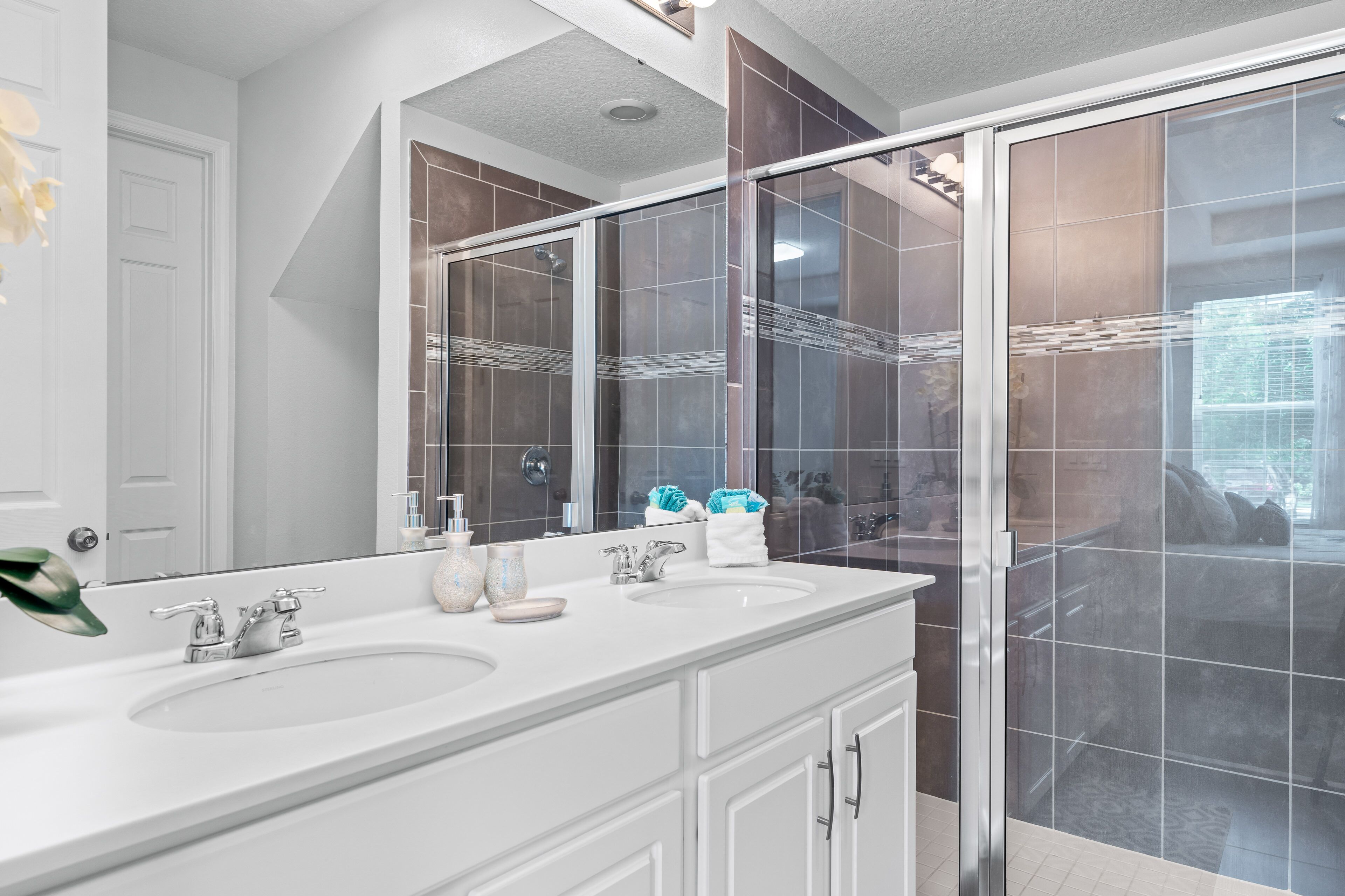 A modern bathroom with two sinks, a large mirror, and a glass shower enclosure.