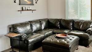 Um sofá modular com uma mesinha de madeira, um tabuleiro decorativo, arandelas na parede e um quadro emoldurado sobre um painel branco.