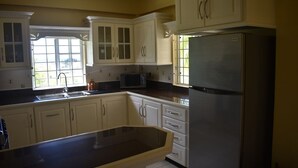 Cozinha com armários brancos, geladeira de aço inoxidável, micro-ondas e janela que oferece iluminação natural.