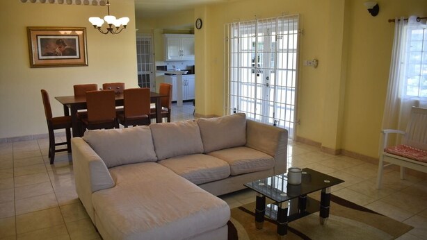 Uma sala de estar com um sofá modular bege, uma mesa de centro de vidro e um espaço de jantar com mesa e cadeiras brancas.