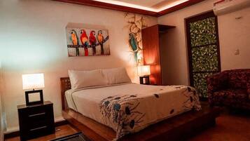 A bedroom with a bed, bedside tables, a lamp, a chair, and a wall with a bird painting.