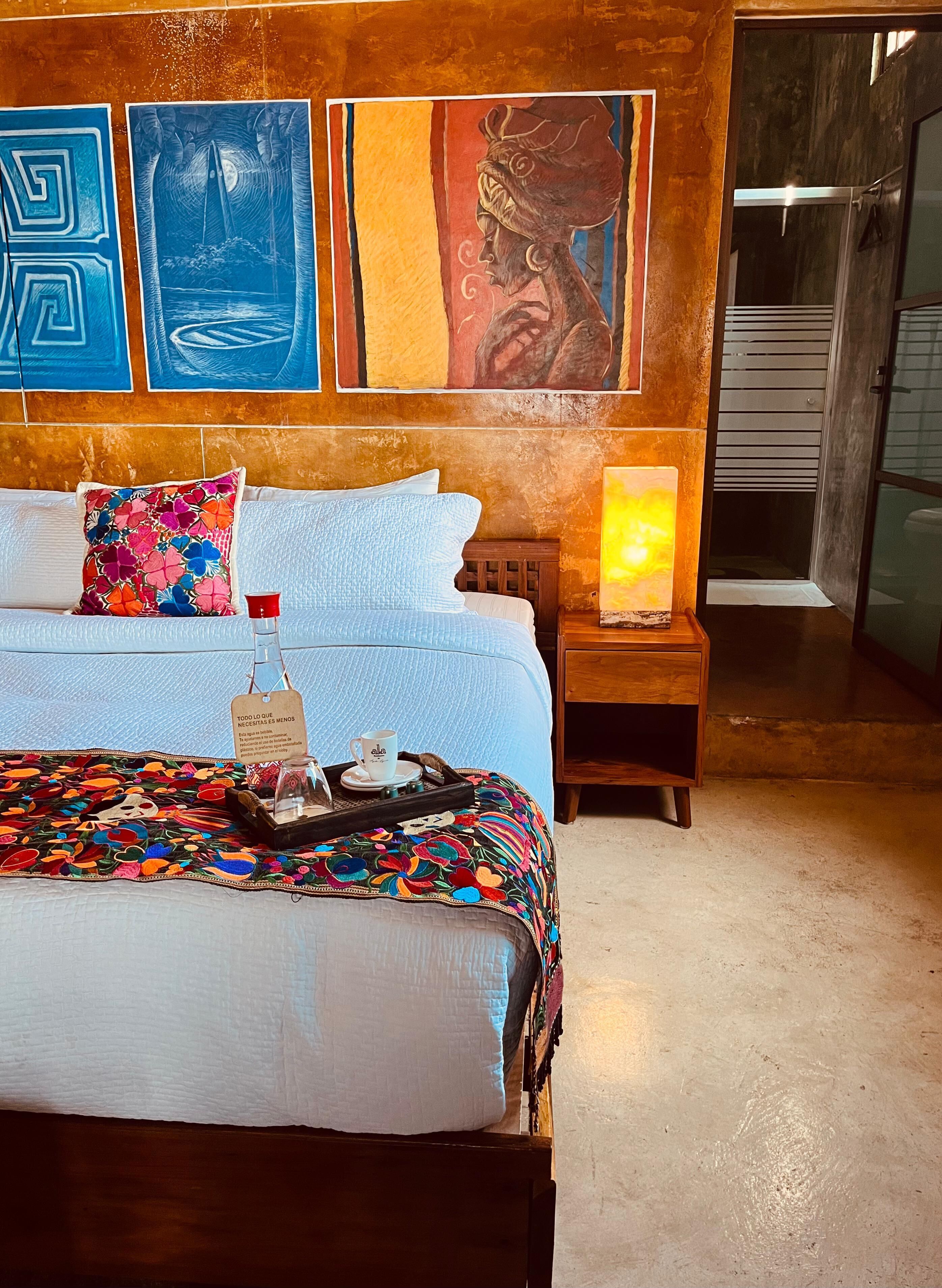 Un dormitorio con cama, almohadas, una mesita de noche, lámpara y una obra de arte en la pared.