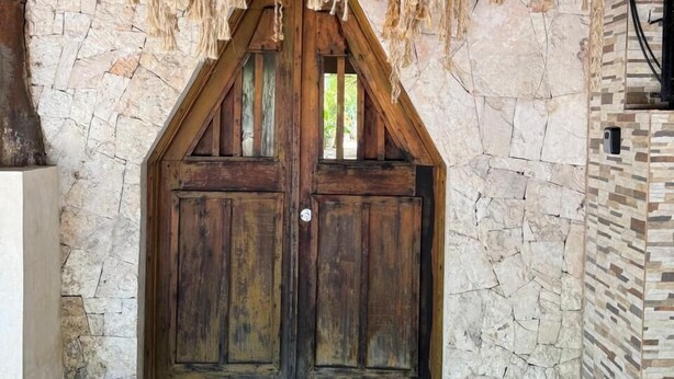 A rustic wooden door with a stone wall backdrop and a thatched roof above. - ALA Residencias (Chetumal)
