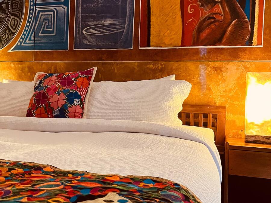 Un letto con una coperta colorata a fiori, un cuscino bianco e una testiera. Sopra il letto, tre opere d'arte incorniciate appese al muro.