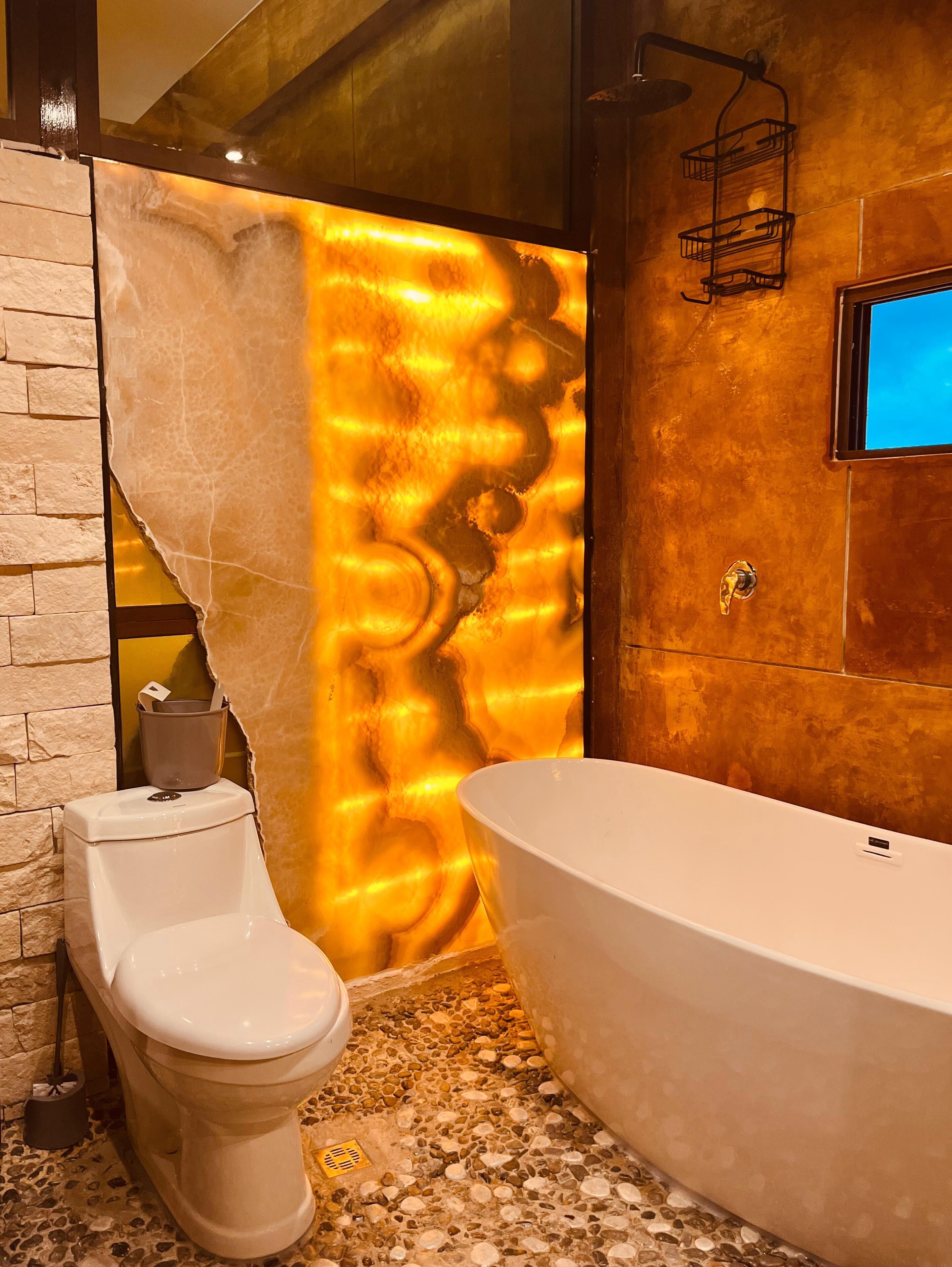 A bathroom with a white bathtub, a toilet, and a textured wall.