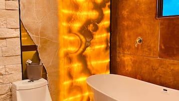 A bathroom with a white bathtub, a toilet, and a textured wall.