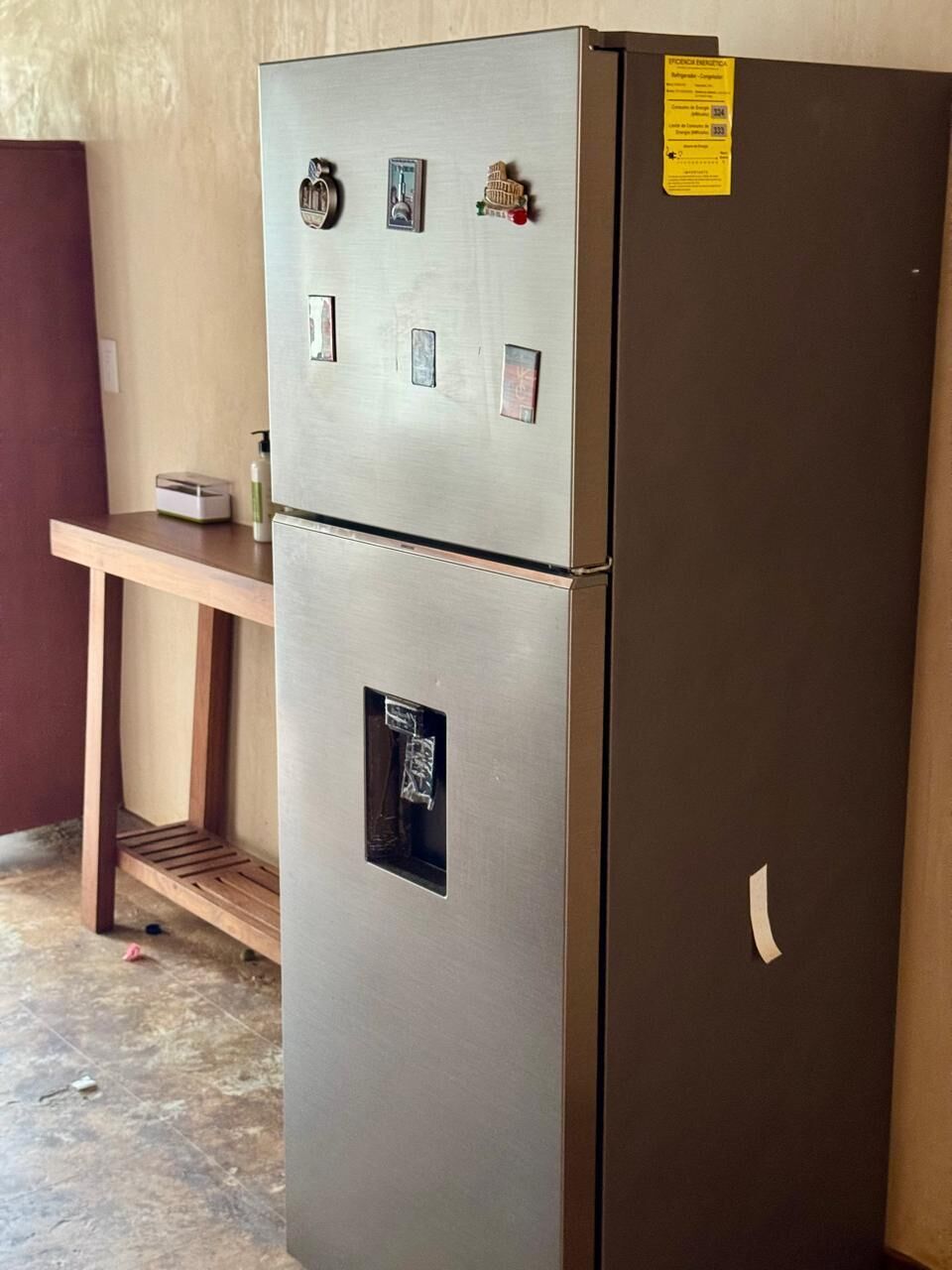 Een roestvrijstalen koelkast met een vriesvak, een bedieningspaneel met knoppen en een klein sticker aan de bovenkant.
