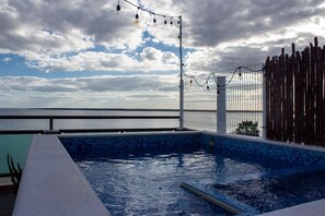 Una piscina con vista al mar, una valla de madera y luces colgantes.