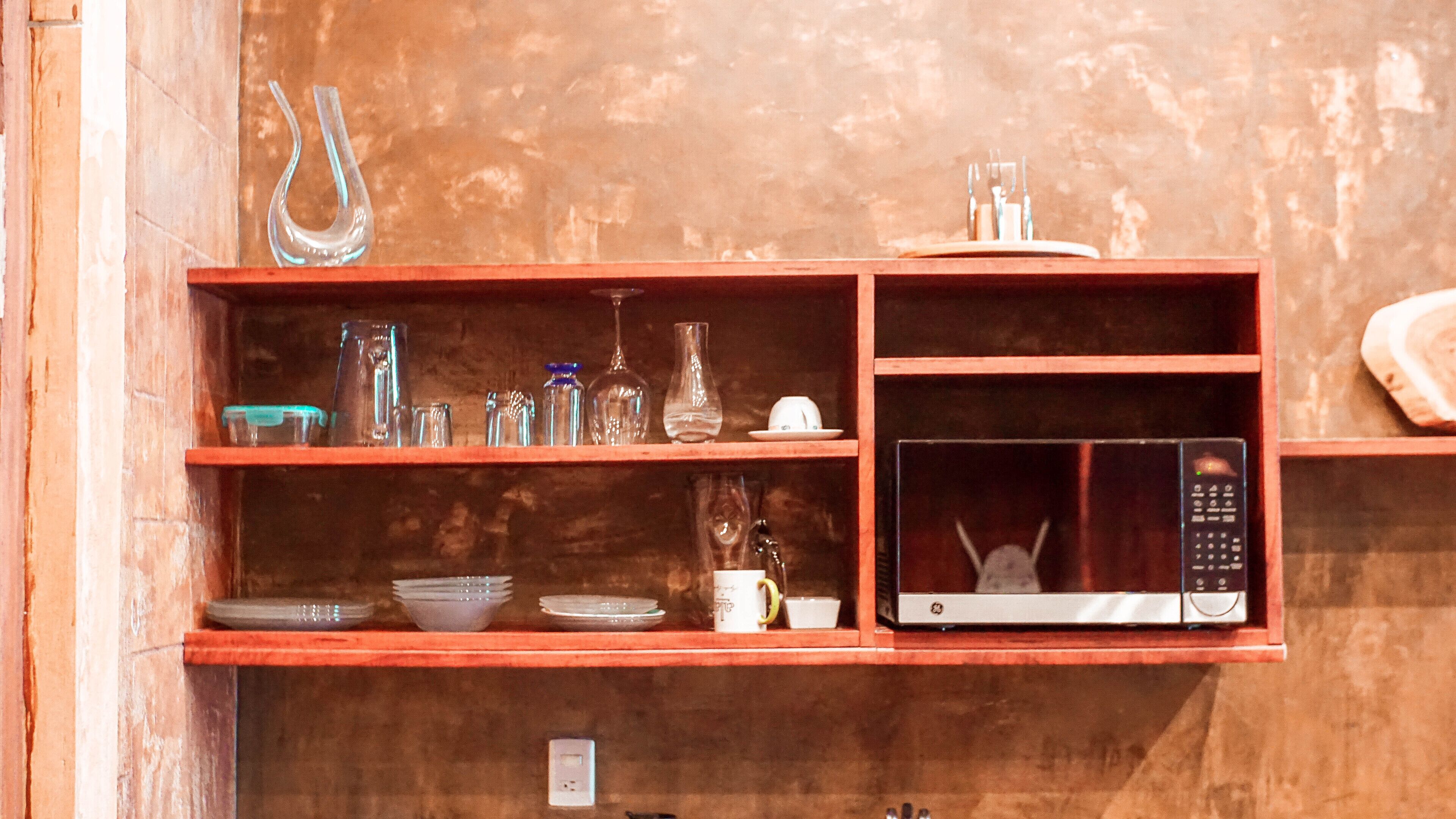 A wooden shelf with various glassware and a microwave.