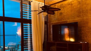 A modern living room with a large TV, comfortable seating, a ceiling fan, and a view of the cityscape through large windows. - ALA Residencias (Chetumal)