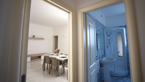 A modern interior with a dining area featuring a white table and chairs, a vase with flowers, and a hallway leading to a bathroom with a shower and toilet. - Gallipoli Italy Luxury Residence (Gallipoli)