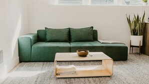 A green sofa with a bowl on a wooden tray, a white chair, and a potted plant in a room with a window and a radiator. - Rose House (Seattle)