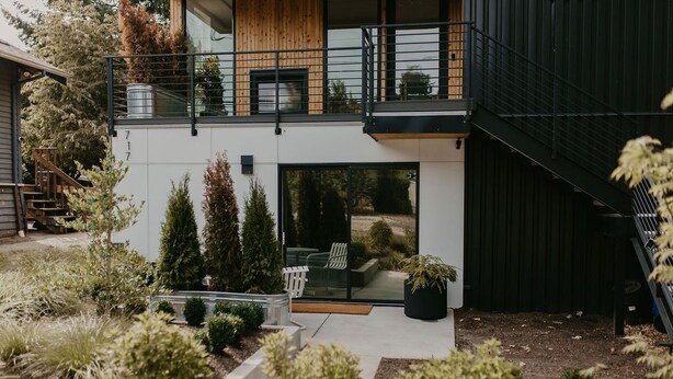 A modern two-story house with a balcony, a small outdoor seating area, and a staircase leading to the upper floor. - Rose House (Seattle)