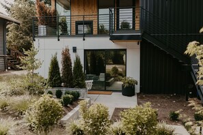 A modern two-story house with a balcony, a small outdoor seating area, and a staircase leading to the upper floor. - Rose House (Seattle)