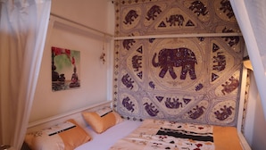 Un dormitorio con cama, almohadas, mesita de noche y un tapiz con motivos de elefantes.