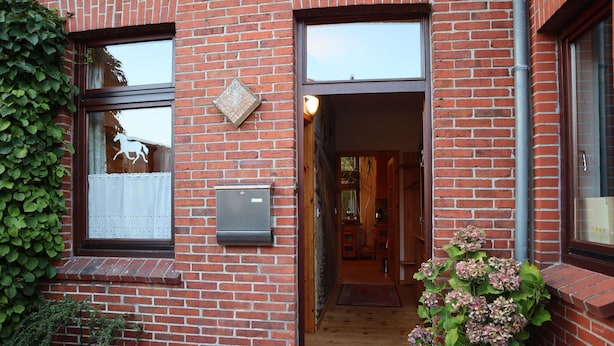 Entrada de un edificio de ladrillo con una puerta de madera, un buzón y una maceta con flores.