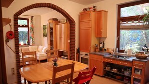 Una cocina acogedora con armarios de madera, una mesa de comedor y una silla roja. Se ve vegetación a través de la ventana.