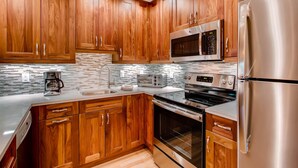 A modern kitchen with wooden cabinets, stainless steel appliances, a microwave, toaster, and a coffee maker. - Westwind 108 2BD 2BA Platinum Condo in Lionshead Village (Vail)