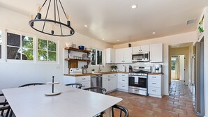 A modern kitchen with white cabinets, a large island, and a dining area with chairs. - Completely Renovated Old Time Los Alamos Home-- with recreation Barn! (Los Alamos)
