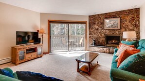 Una sala de estar con televisor, chimenea, pared de piedra y puerta corrediza de vidrio al exterior.