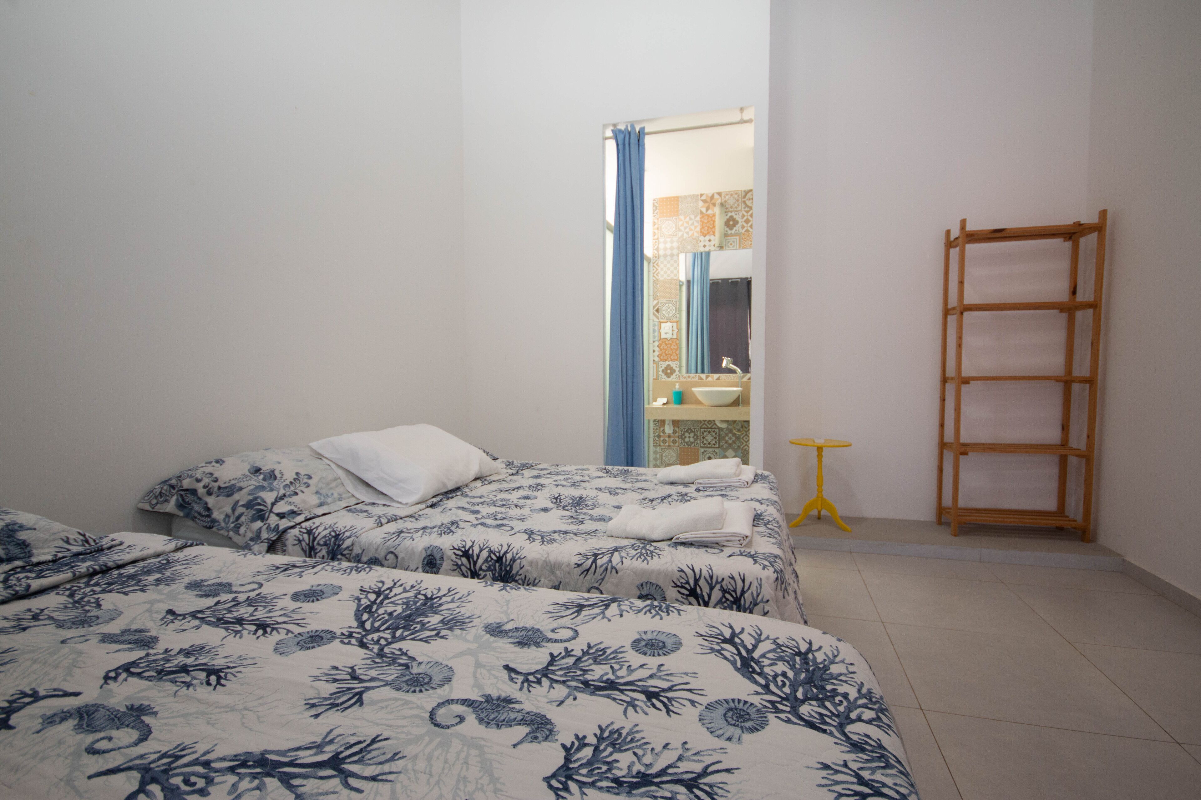 A bedroom with two beds, a bathroom visible through a doorway, and a wooden shelf.