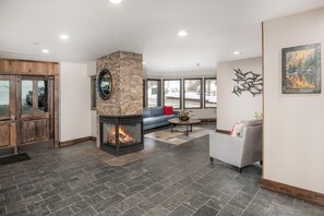 A modern living room with a stone fireplace, a blue sofa, a gray armchair, and a large window.