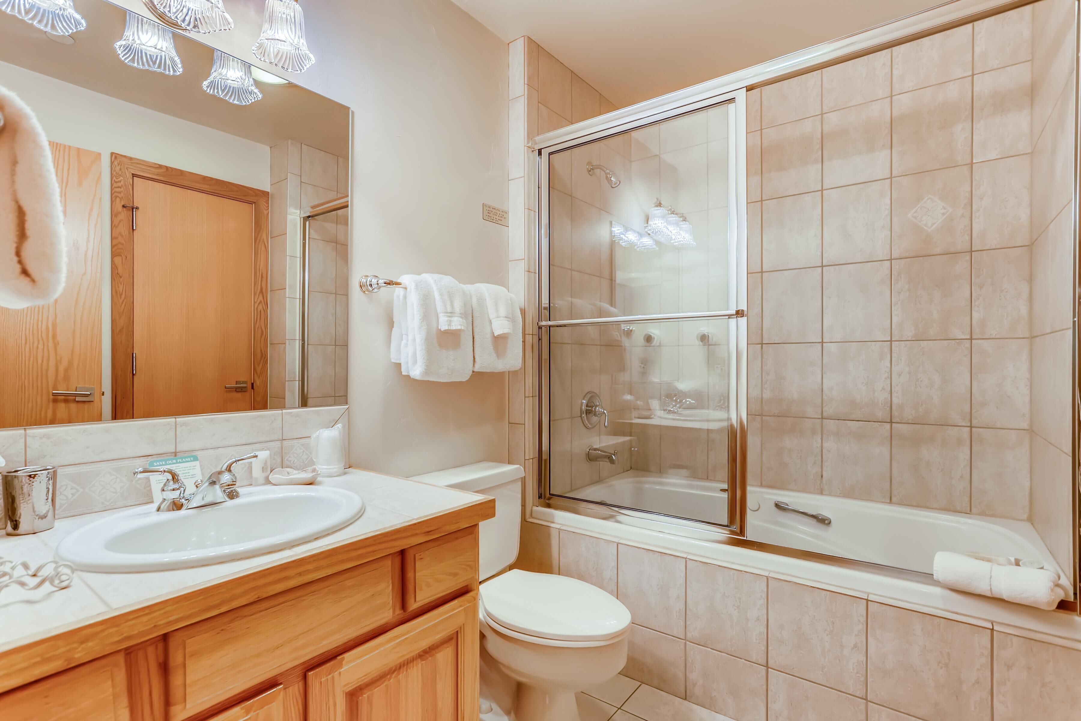 A bathroom with a wooden vanity, a sink, a toilet, and a glass-enclosed shower area.