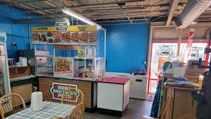 Interior de un restaurante Hunt Brothers Pizza con una pared azul, una vitrina de pizzas, una barra y una mesa con sillas.