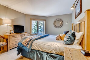 Relax in this serene bedroom with a large bed, nightstand, and TV, offering a peaceful view of the surrounding greenery.