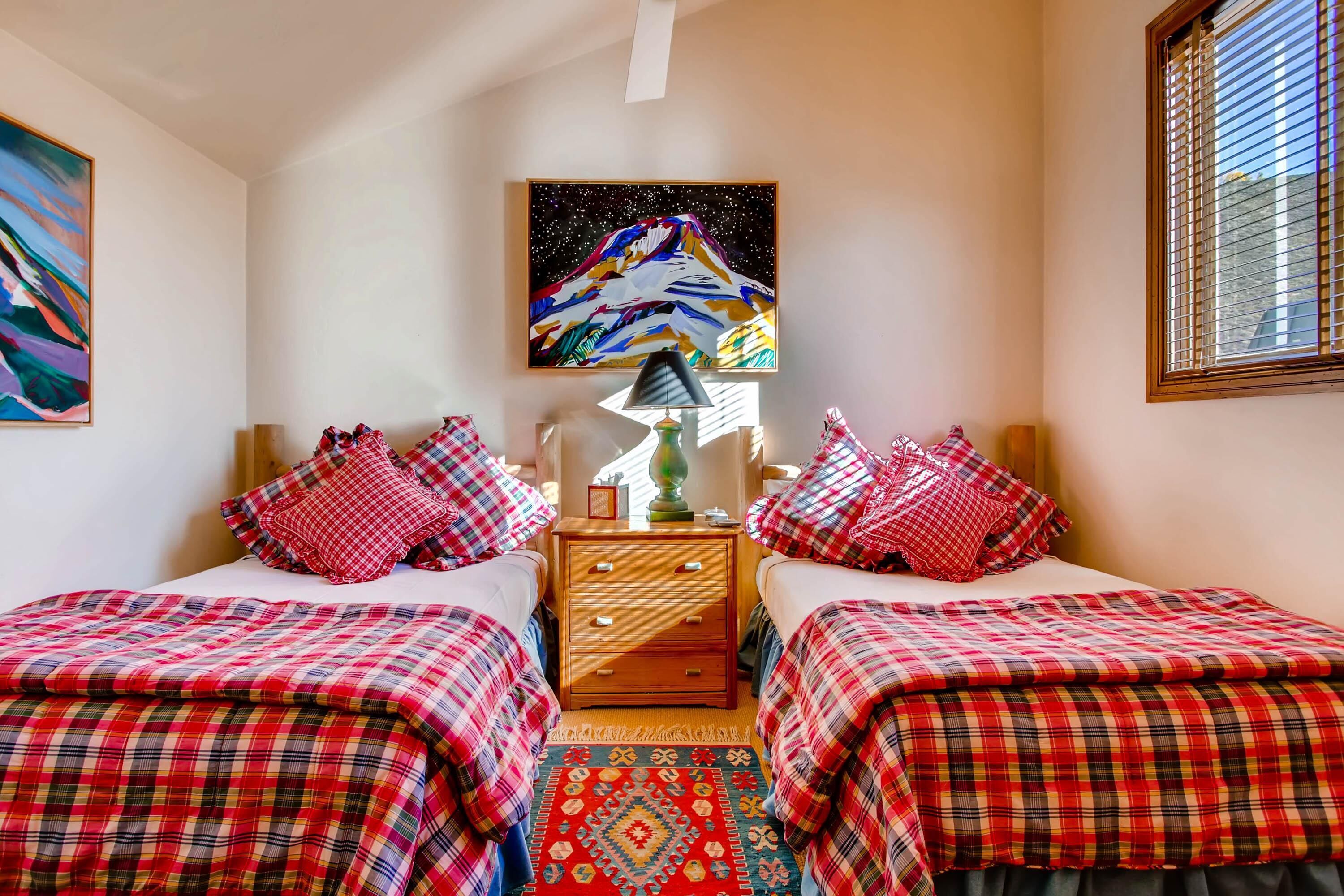 A bedroom with two beds, a nightstand, a lamp, and a painting on the wall.