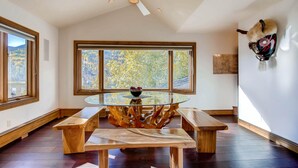 Une pièce spacieuse dotée d’une grande fenêtre, d’un ventilateur de plafond et d’une table ronde en verre, entourée de bancs en bois.