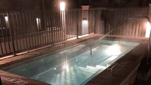 En uppvärmd utomhuspool med en kant av sten och ett metallräcke, omgiven av ett staket.