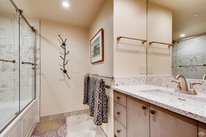 A modern bathroom with a glass shower enclosure, a vanity with a speckled countertop, and a wall-mounted towel rack with patterned towels. - Westwind 303 1BD 1BA Plat. Condo (Vail)