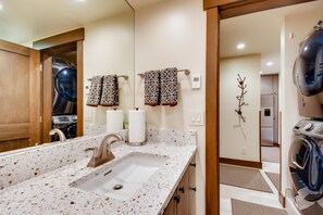 A bathroom with a double sink, a mirror, towels, and a wall-mounted heater. - Westwind 303 1BD 1BA Plat. Condo (Vail)