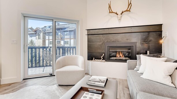 Una sala moderna con chimenea, un sillón blanco, un sofá gris y vistas a un balcón con barandilla.