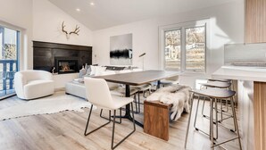 Una sala de estar moderna con chimenea, sofás blancos, una mesa de comedor y un ventanal grande.