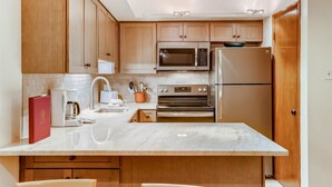 A modern kitchen with wooden cabinets, stainless steel appliances, a marble countertop, and a built-in oven. - Westwind 109 1BD 1.5ba Gold Condo in Lionshead Village (Vail)