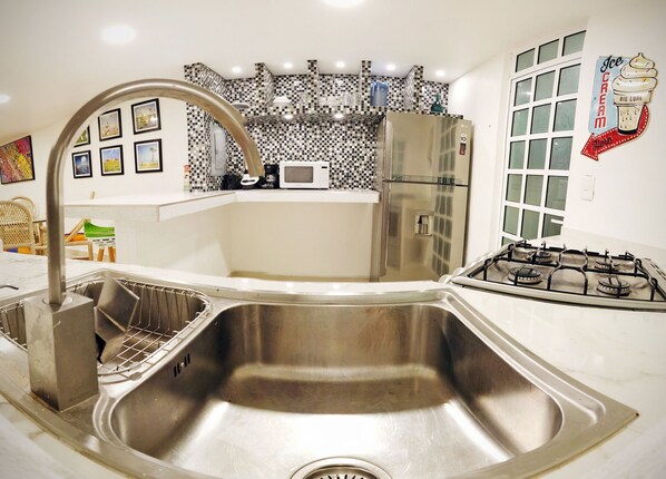 Una cocina moderna con un lavamanos de acero inoxidable, microondas, refrigerador y estufa a gas.