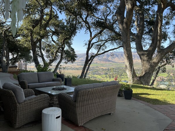 A patio with wicker furniture, a stone fire pit, and a view of a valley and mountains.