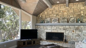 A living room with a stone fireplace, a flat-screen TV, and a leather ottoman.