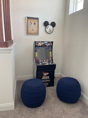 A hallway with a framed picture of cartoon characters, a Mickey Mouse clock, a video game console, and two blue bean bag chairs.