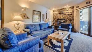 A living room with a stone wall, blue patterned sofas, a wooden coffee table, and a large window. - Westwind 102 2BD 2BA Diamond Condo in Lionshead Village (Vail)