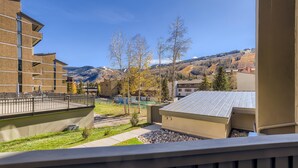 A view from a balcony overlooking a courtyard with a building, trees, and a distant mountain range. - Westwind 102 2BD 2BA Diamond Condo in Lionshead Village (Vail)