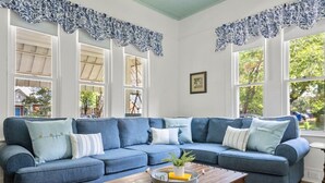 A large blue sectional sofa with multiple pillows, a wooden coffee table with a plant and a tray, and a window with a view of greenery.